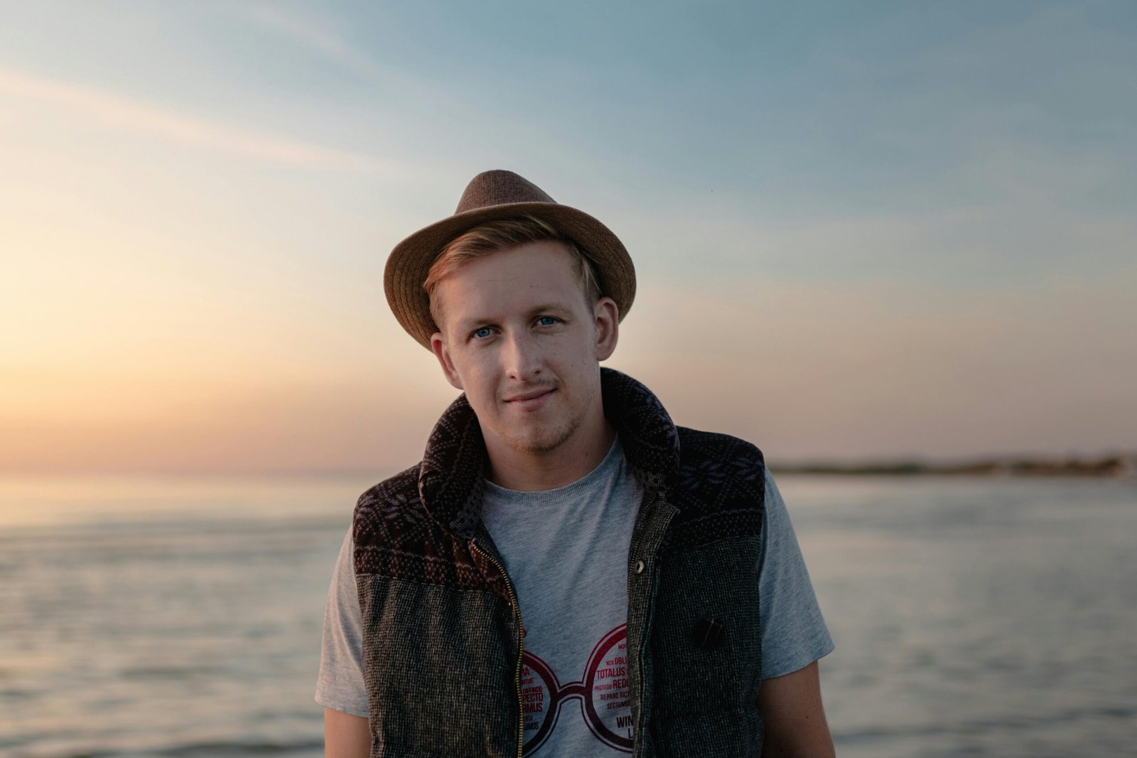 Portrait of a young man with a hat enjoying the serene beach sunset.